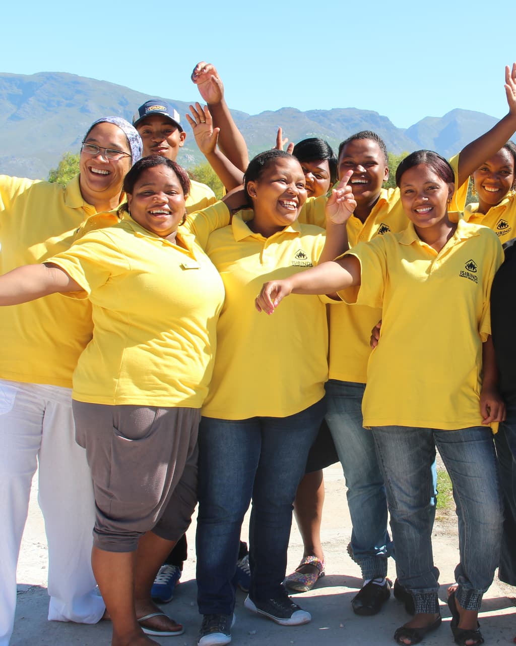 A group of women in matching yellow shirts cheering together with mountains behind them